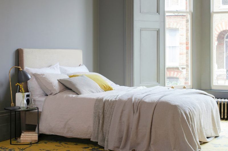 A classic bedroom with floral yellow flooring, a simple bed with neutral linen and tall ceiling.