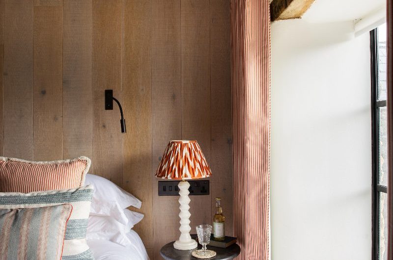A rustic bedroom design with wood wall panelling and matching flooring, with a window seat and minimalist decor.