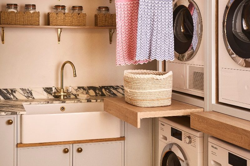 A utility room with pale blue cabinets, stacked double laundry appliances, statement marble, and clever storage.