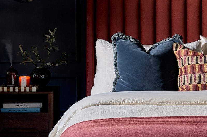 A moody bedroom with red velvet headboard, dark paint, and luxurious furniture.