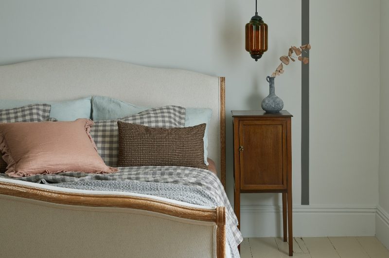 A calming bedroom drenched in sage green with a simple bed frame, gingham bedding, and a compact wood beside table.