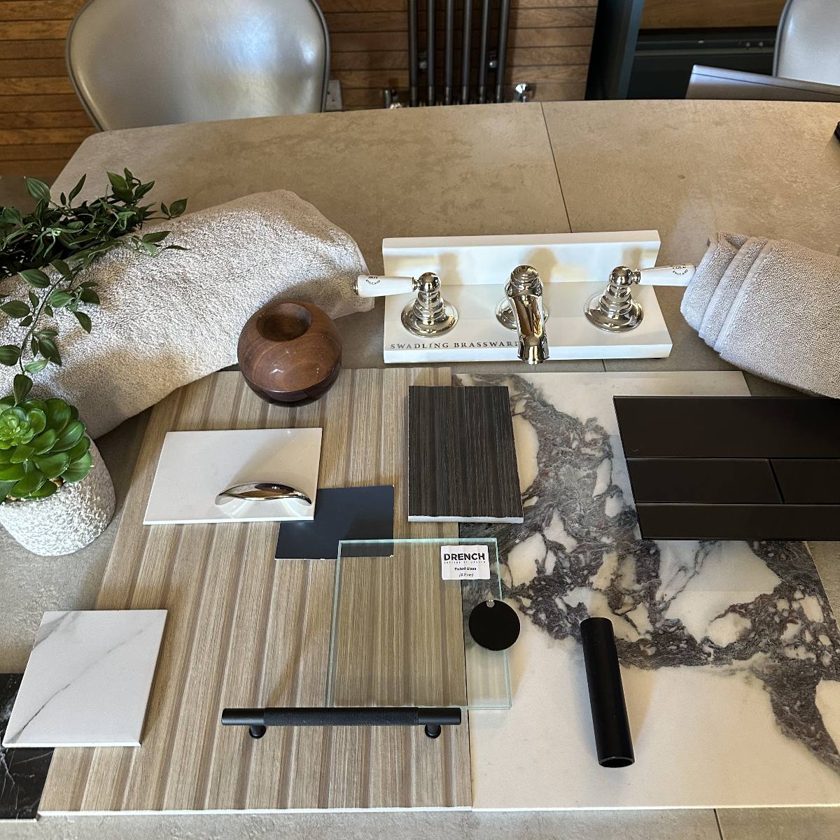 A moodboard at a bathroom showroom with wood and stone samples, classic brassware, and dark finishes.