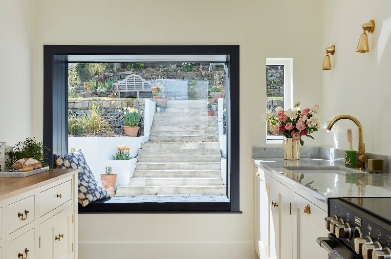 A white kitchen design with classic cabinetry, a black range cooker, brass tap and lighting, and a window nook with a painted border.