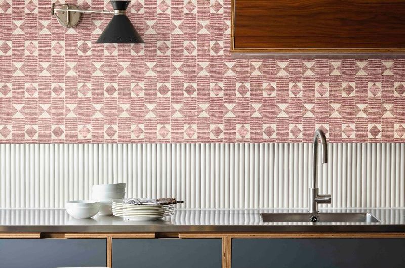 A simple kitchen design with dark blue base units, fluted splashback, stainless steel worktop and a flag patterned wallpaper.
