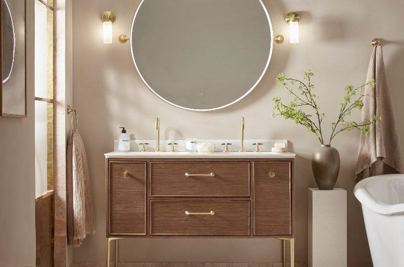 A modern bathroom with a freestanding wood vanity with double basins, a large circular mirror and textured floor tiles in an undulating pattern.