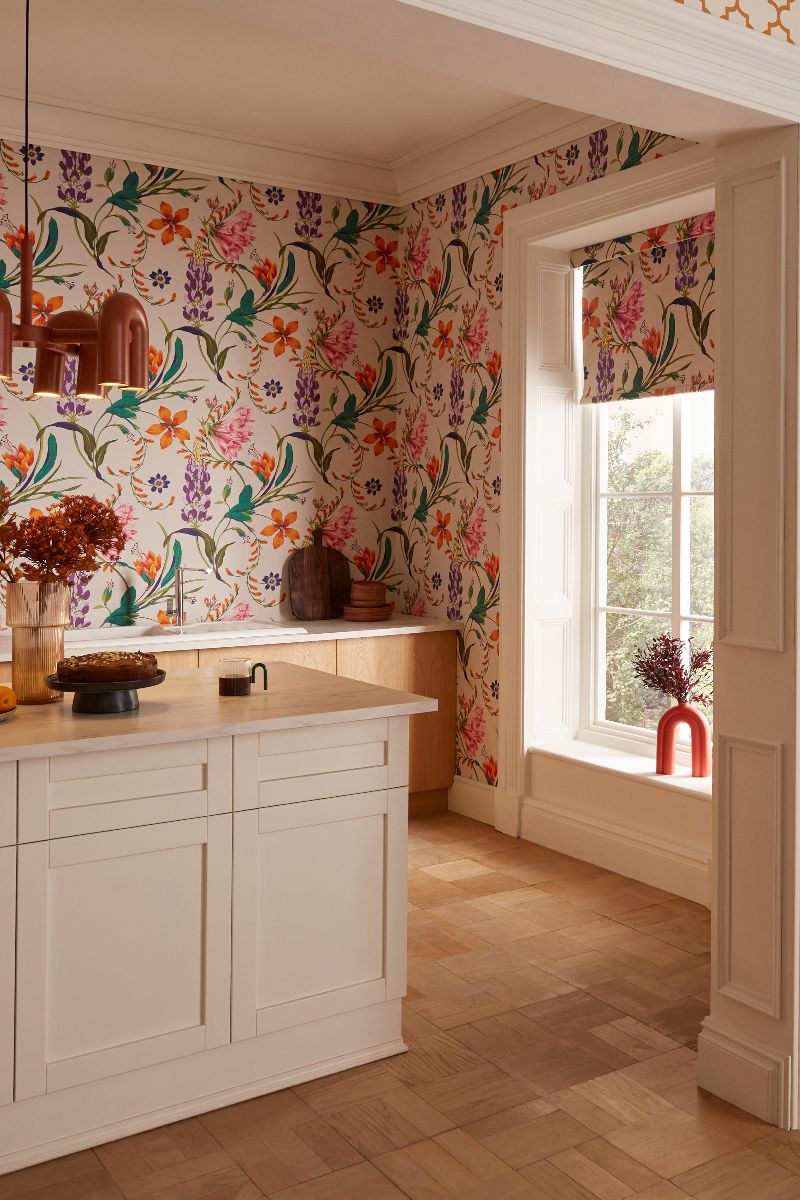 A white and wood cooking space with floral wallcoverings and matching roller blind, and wood flooring.
