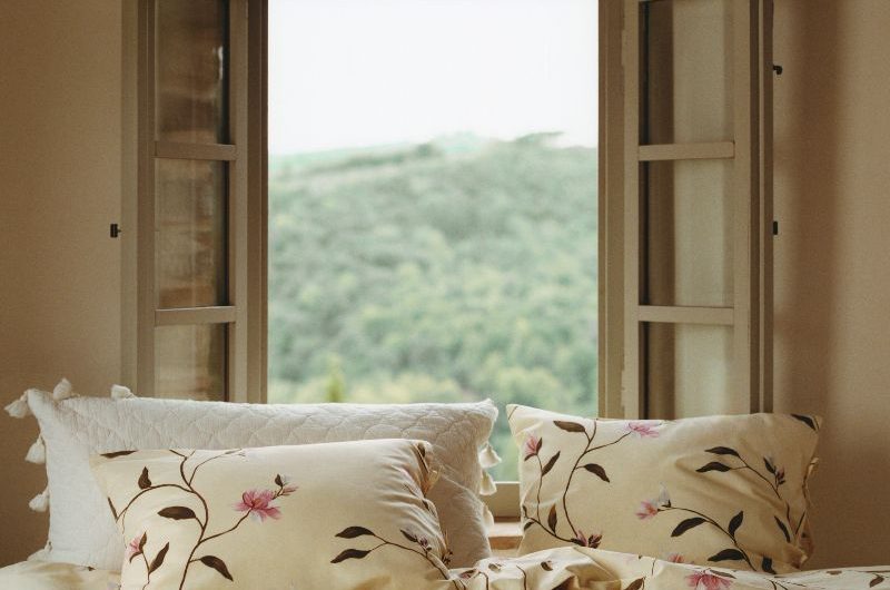 A neutral sleep space with neutral and floral bedding in front of an open window.
