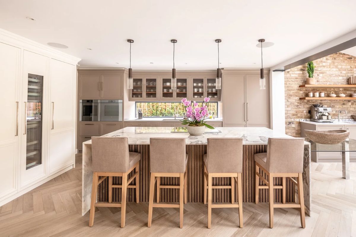 A classic scheme with timeless cabinetry painted in neutral shades and a central island with a fluted base and stone worktop with waterfall edges.
