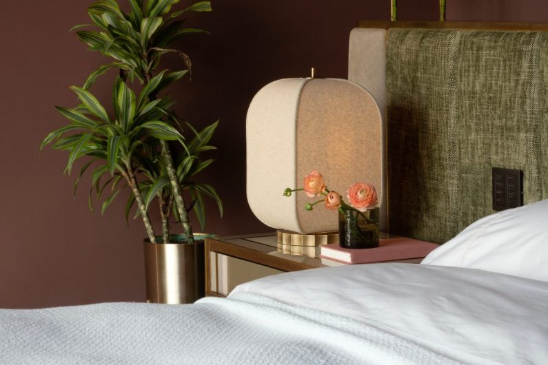 Closeup at a luxurious bedroom bedside table with a tactile lamp, house plants, and dainty decor.
