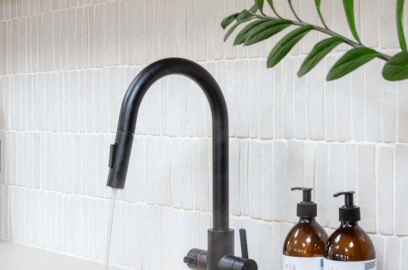Closeup at a black boiling-water tap with an inset sink, and kit-kat splashback tiles.