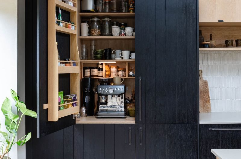An open, double-door pantry cupboard with coffee machine, breakfast essentials, and a door-mounted rack.