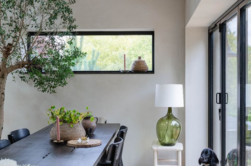 A calm dining room with a wood table, dark wood chairs, microcement flooring, and large glazing.