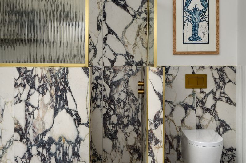 A boutique bathroom design with statement marble surfaces, white sanitaryware, fluted glass and brass panels.