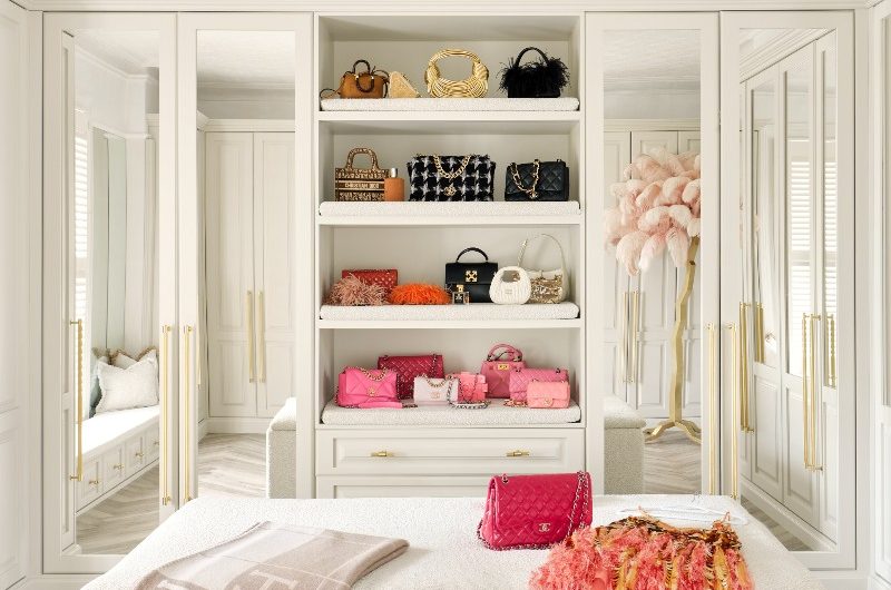 A glamorous dressing room with bespoke wardrobes and open storage, plus an ottoman upholstered in boucle.
