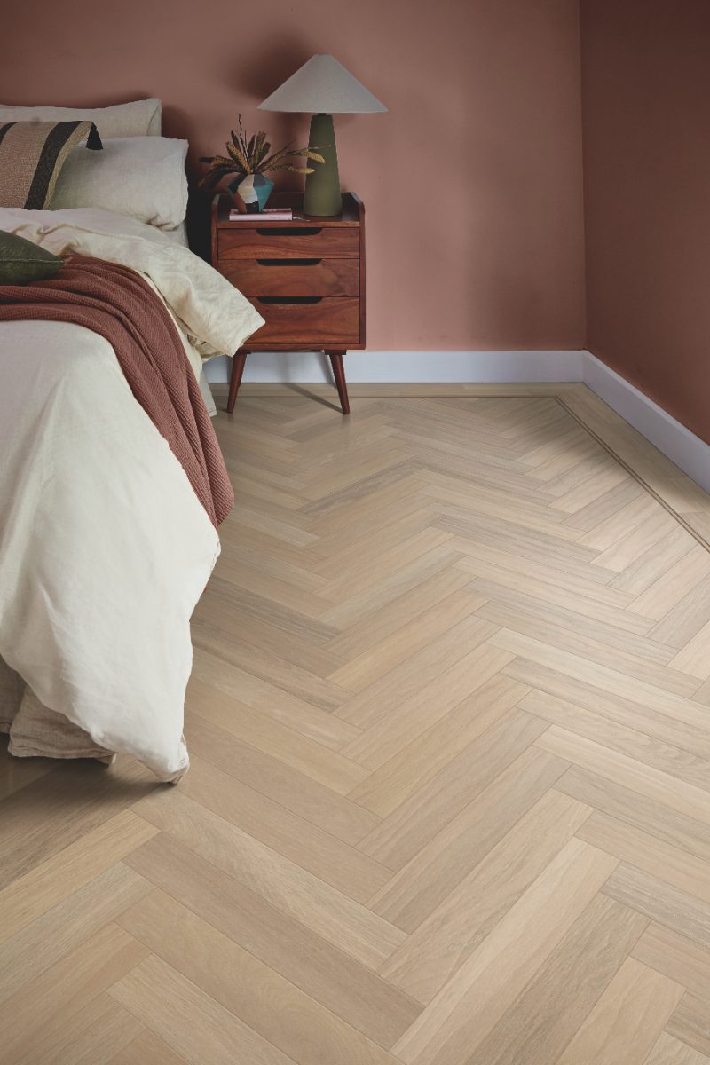A bedroom design with herringbone wood flooring with a decorative border, distinct paint colour on the skirting and a terracotta shade on the wall.