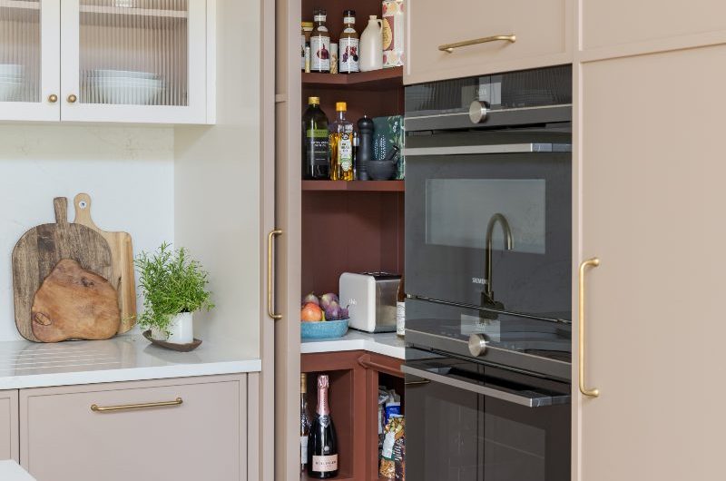 A neutral kitchen design with built-in appliances and a walk-in pantry hidden behind sliding doors.