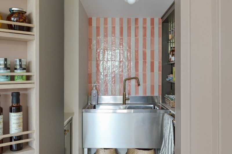 A wash zone in a secondary kitchen with striped wall tiles, a stainless steel sink and brass tap.
