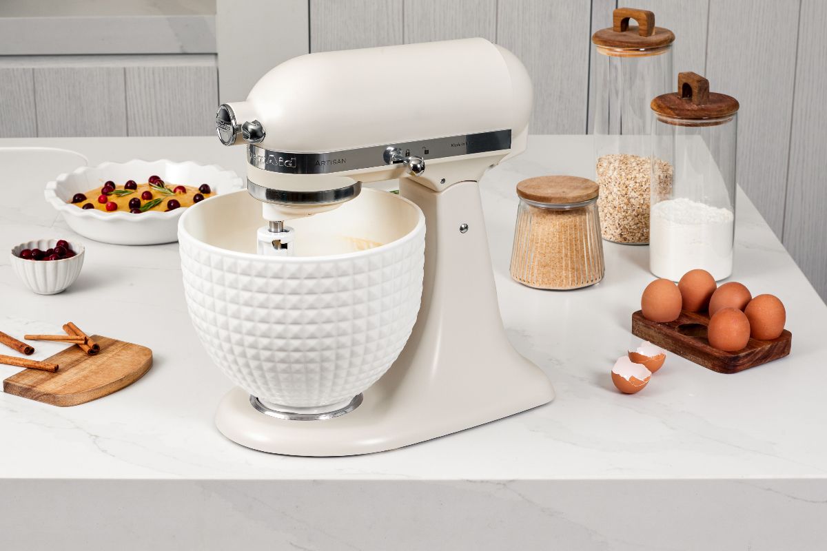 A white veiny countertop with a mixer, baking ingredients, and ceramic dishes.