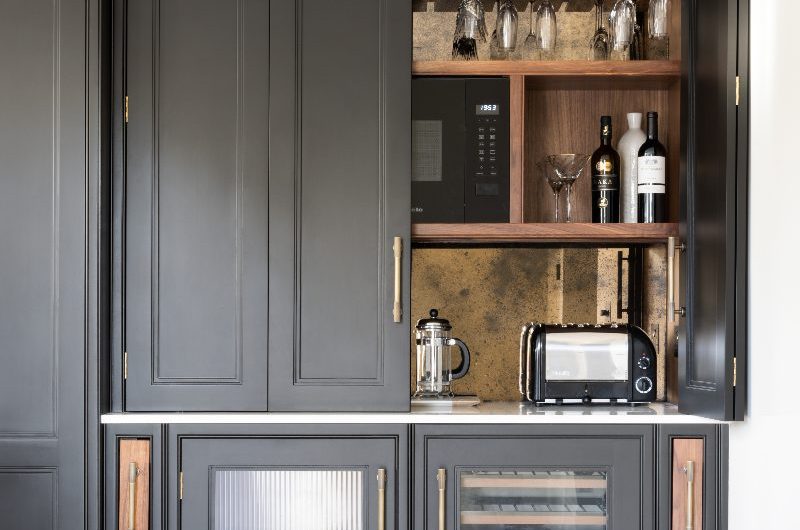 A drinks cabinet with wood interiors and aged splashback, with a built-in bottle fridge and bi-fold doors.