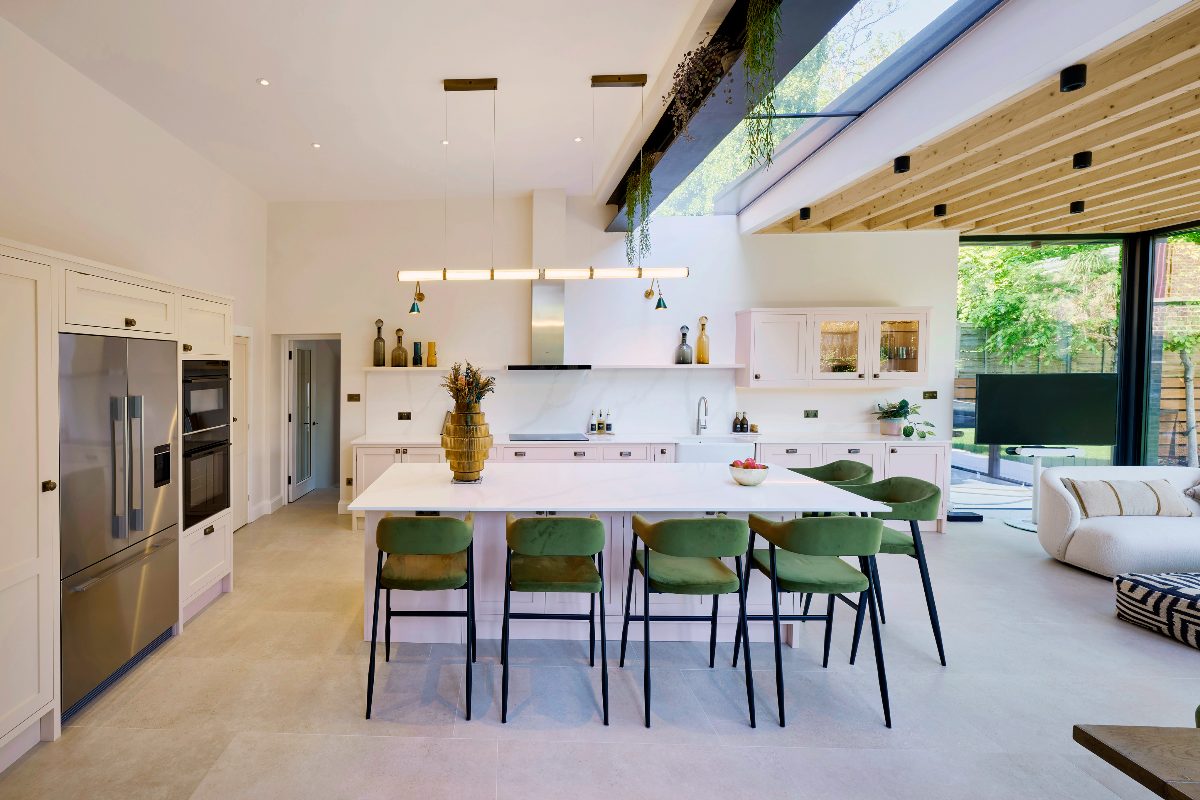 View of the pink kitchen layout with a central island, glazing, and houseplants hanging down from the RSJ beams.