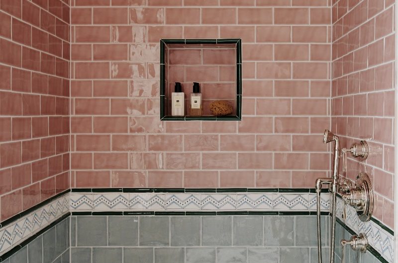 A striking shower area with classic sanitaryware, a marble tray, pink metro tiles on the upper half of the wall with a matching niche, a decorative border, and square sage green tiles on the bottom half of the walls.