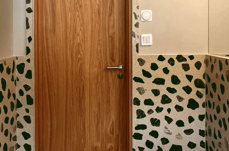 A bathroom design with oversized terrazzo surfaces, simple sanitaryware, and a wooden door.