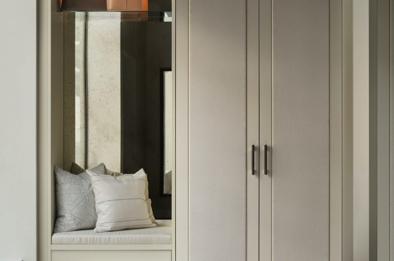 Closeup at a dressing area with bespoke wardrobes, a tall mirror, and a nook with a handy seat.