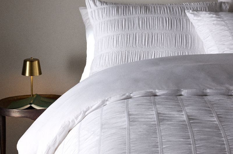 A simple, luxurious scheme with white seersucker bed linen, a minimalist side table, and wall art.