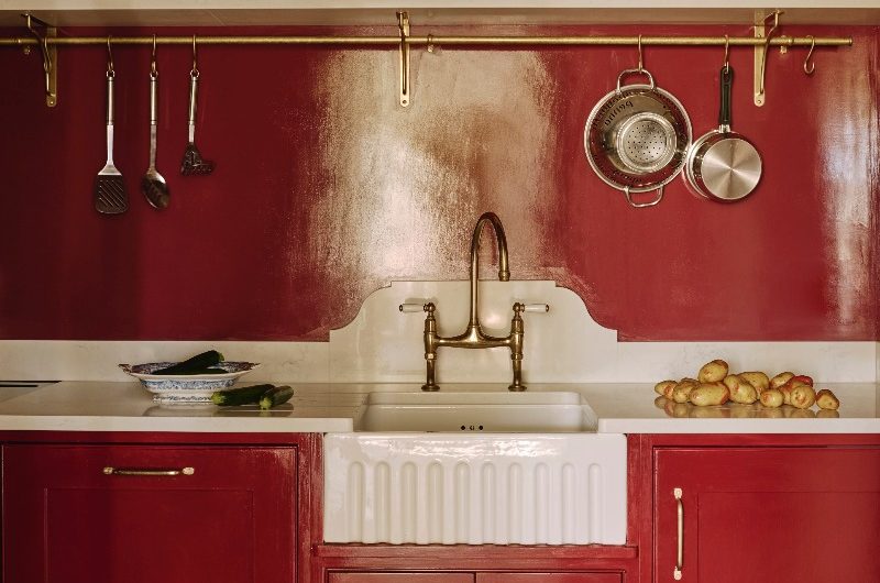 A dark red pantry with a glossy splashback, butler sink, classic cabinetry and open shelving for displaying decor.