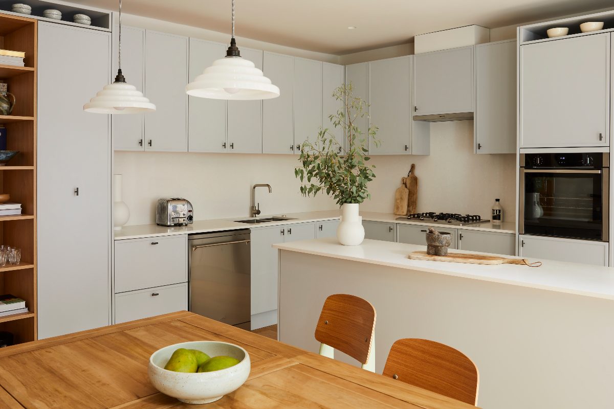 A neutral kitchen with an L-shaped layout with a narrow peninsula, with slim Shaker cabinets, chrome and stainless steel fittings and fixtures and an adjoining dining area.