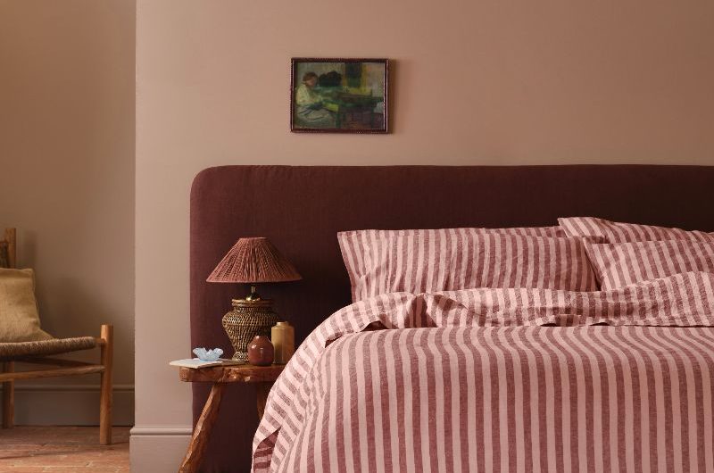 A calm, rustic sleep space with terracotta flooring, an extra large headboard, and striped bed linen.