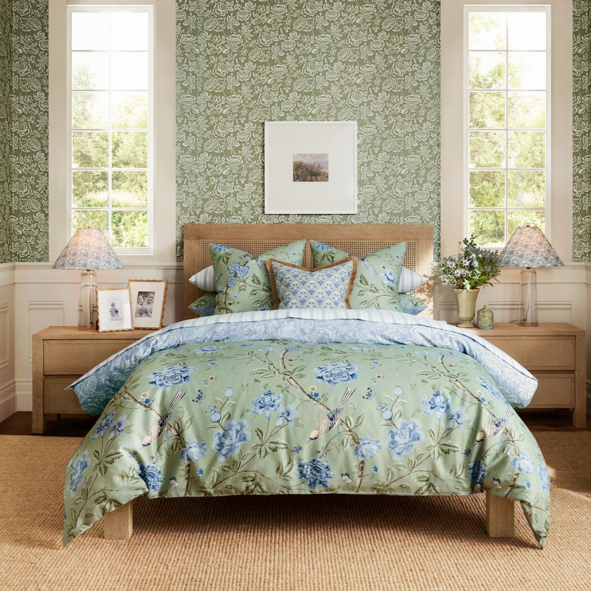 A green sleep space with wood and rattan furniture, a jute rug, green linen, nature-inspired wallpaper, and bedside lamps.