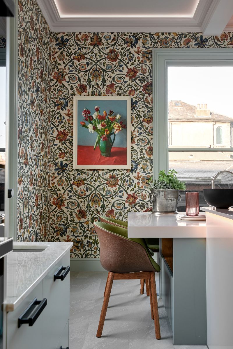 A dining zone with a central island with seating, botanical prints on the walls, and pale blue cabinetry.