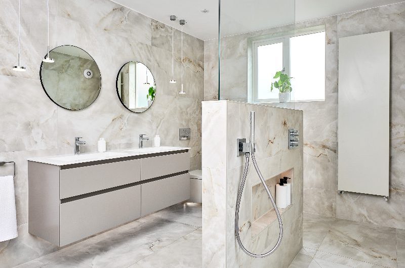 A large, neutral couple's bathroom with a double vanity and an open walk-in shower with a dividing wall for a sense of privacy.
