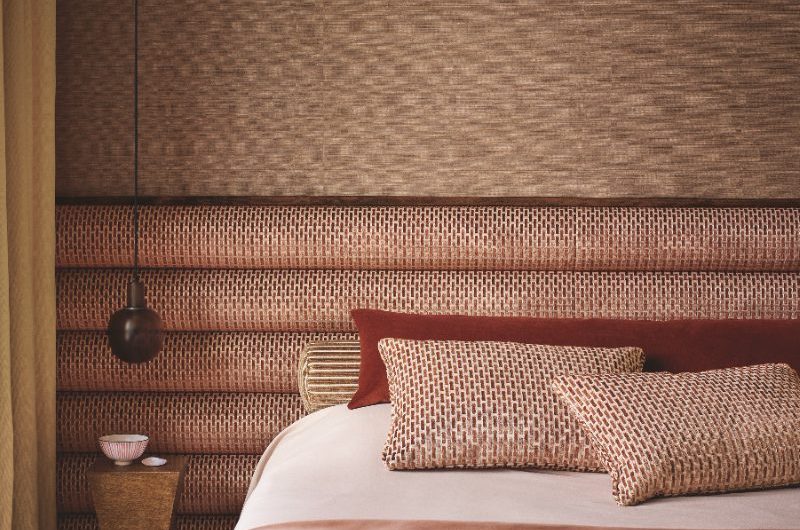 A luxurious bedroom with a tactile wallpaper, extra long fabric headboard, and soft furnishings.