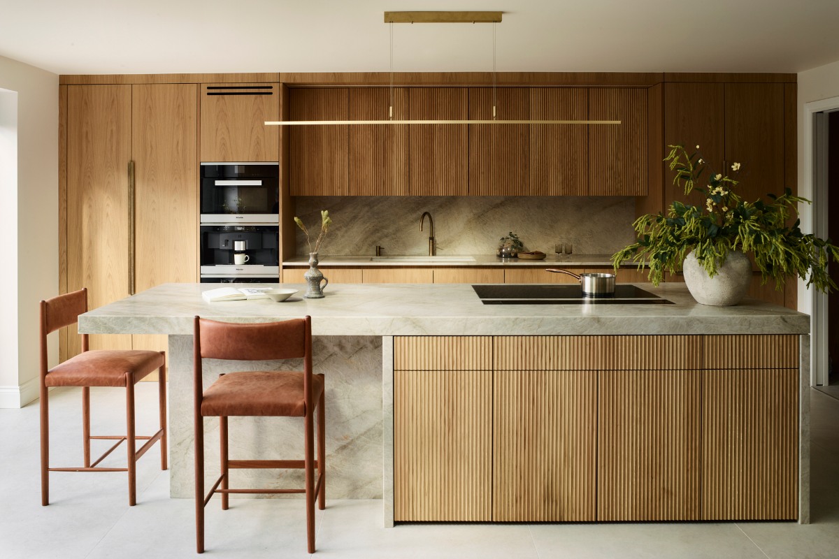 A modern kitchen design with floor-to-ceiling cabinetry, a central island clad in stone with fluted cabinets, a hob, and seating.