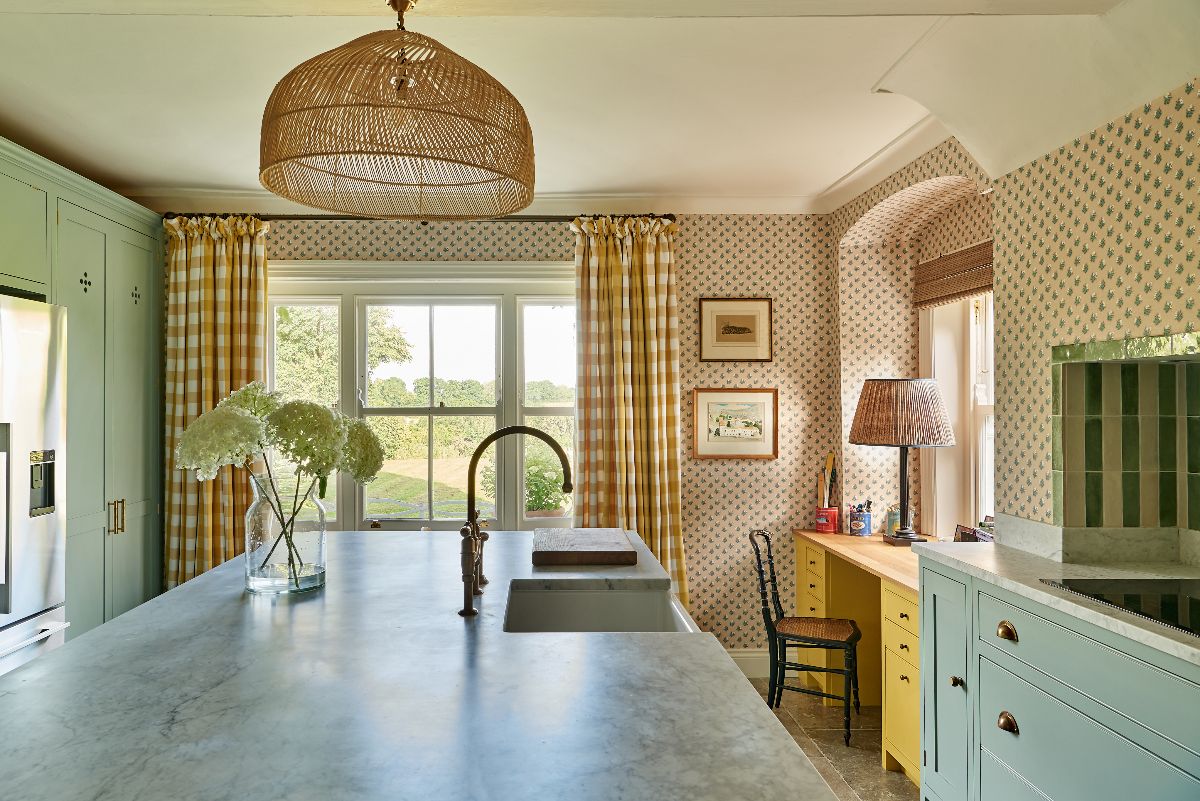 A classic kitchen with tall light blue cabinets with vent holes, a central island, checkered curtains, and acorn patterned wallpaper.