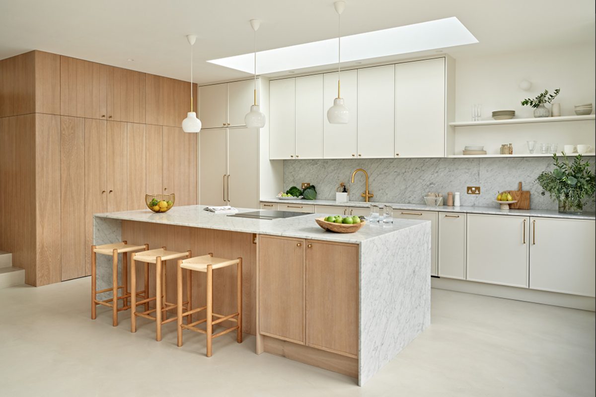 A Scandi-style kitchen design with slim-Shaker cabinetry in a warm neutral colour, with an island, oak finishes, and layered lighting.