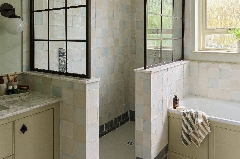 A modern bathroom design with a fitted tub and a semi-open shower with zellige tiles and steel-framed glazing installed above the half walls.