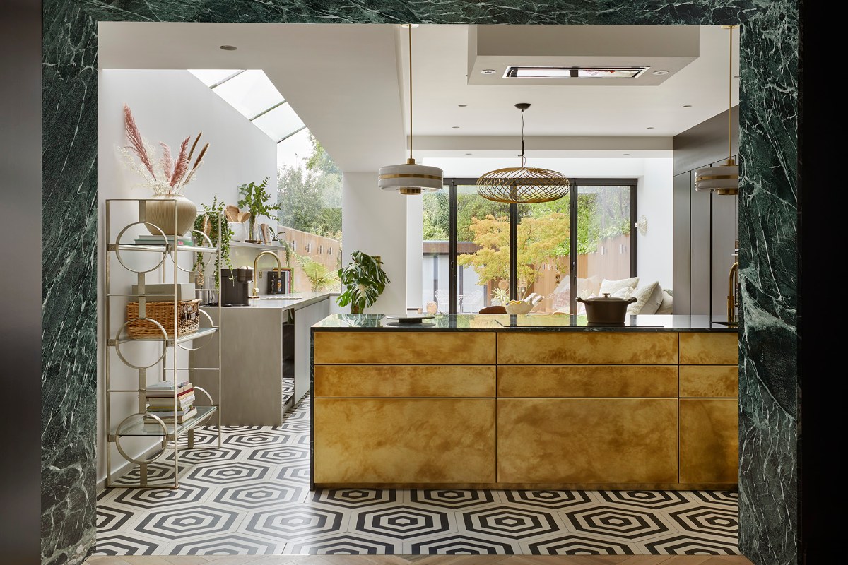 View of a modern kitchen design with geometric flooring, a statement metallic island, and a green stone entryway border.