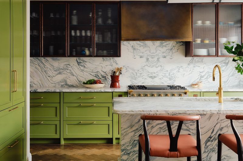 A statement kitchen design with green base units, wood and reeded glass wall cabinets, and mixed materials and finishes, from the opulent marble island, to the gold tap, and burnished brass extractor hood.