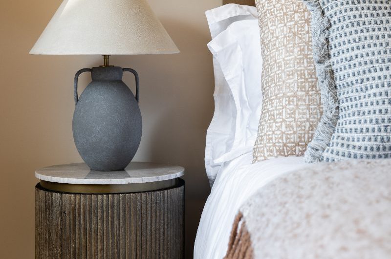Closeup at a bedside table with fluted wood and topped with marble, with a timeless lamp on top of it.