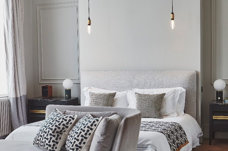 A grey bedroom design with luxurious textiles on the bed, layered lighting, and a velvet lounging area.