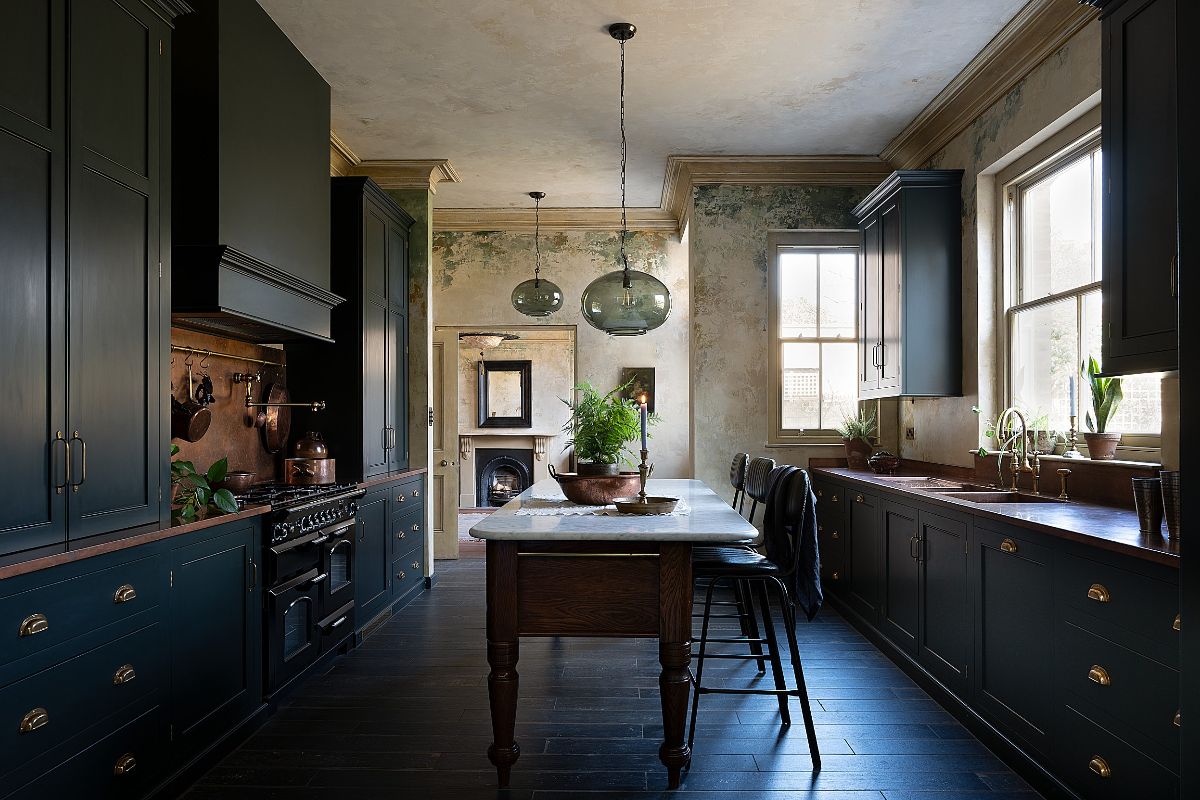 A kitchen design with dark green Shaker cabinets, dark wood flooring, wallpaper decor, and a baker's table in an old London townhouse.