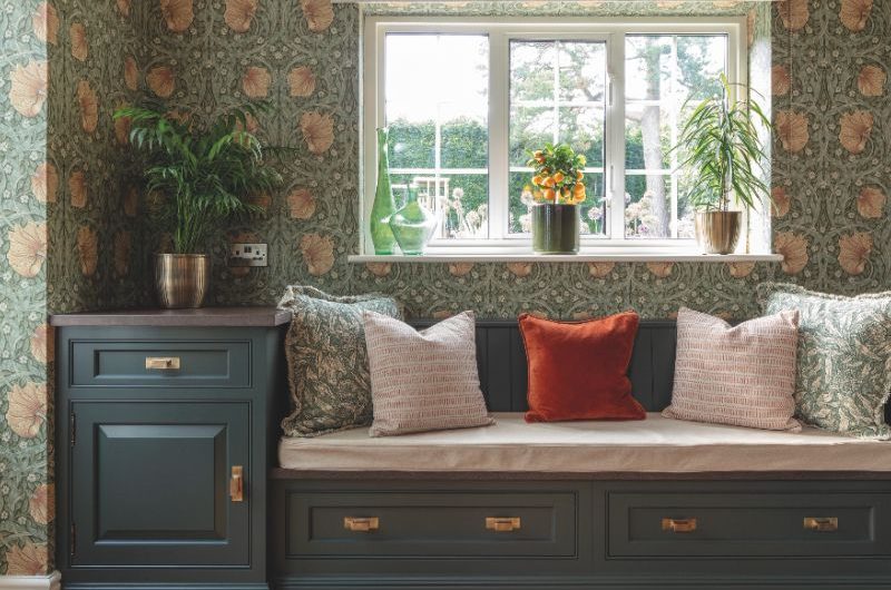 A seating nook by a window with dark green furniture and herringbone flooring.
