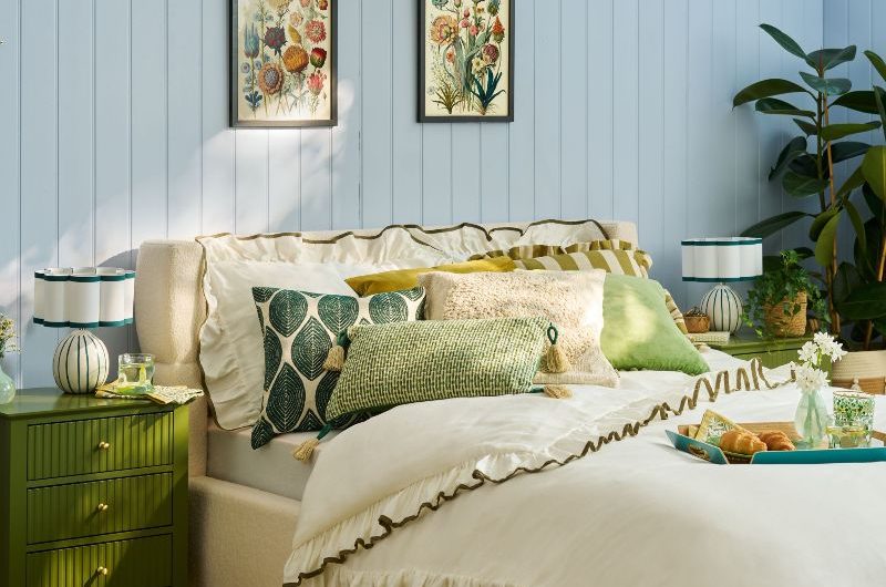 A blue sleep space with simple white linen with green ruffles, nature-inspired decor, green side tables, and house plants.