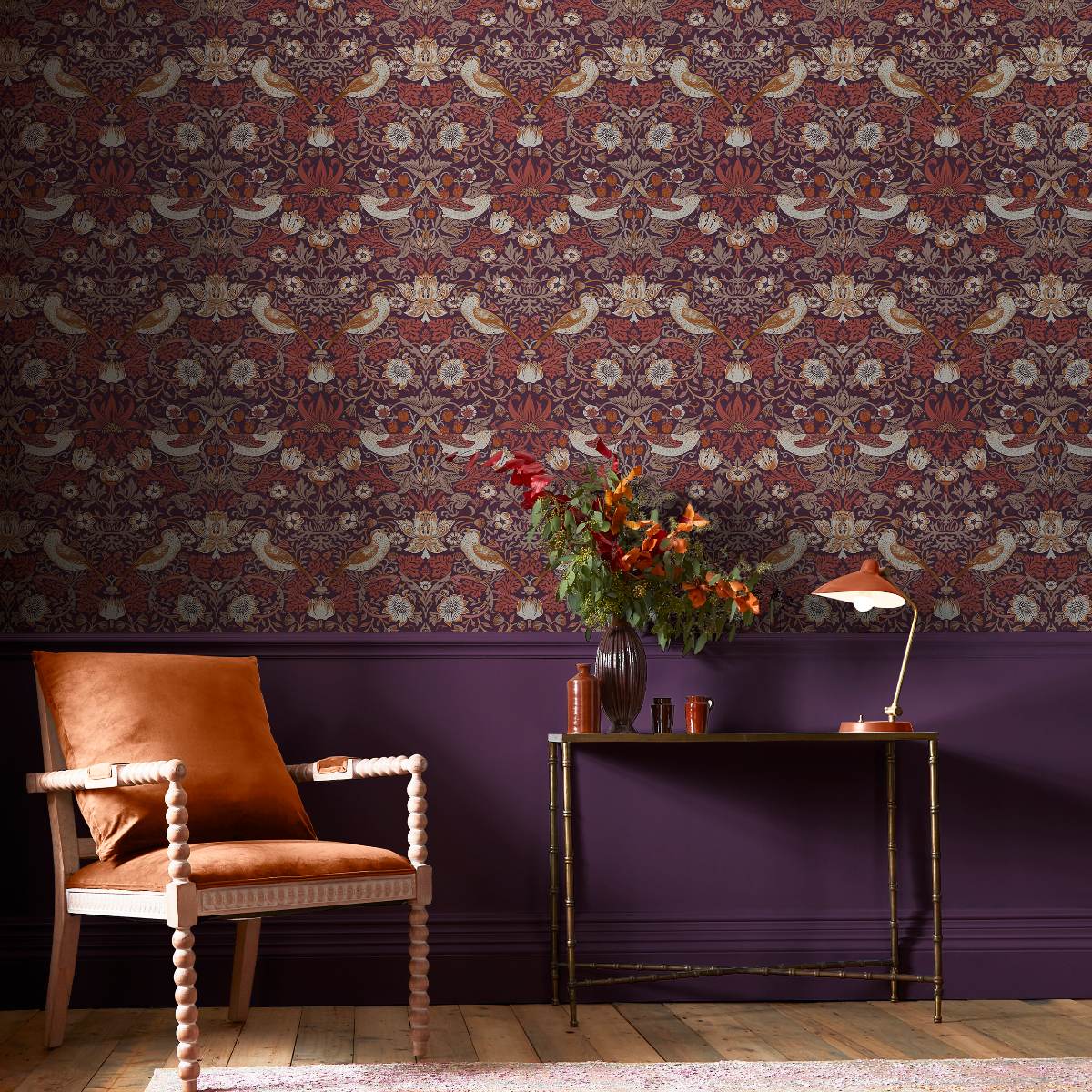 A classic scheme with purple panelling, William Morris wallpaper, bobbin armchair, and a brass console table.