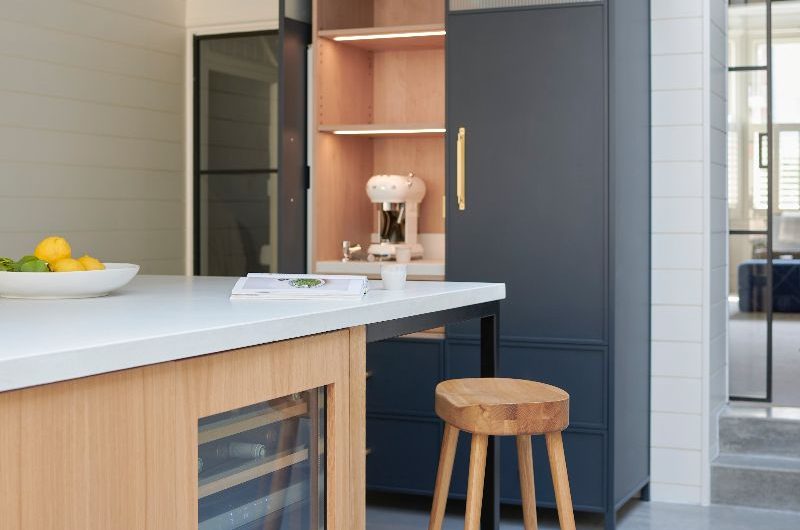 A breakfast cupboard with pocket doors and LED strips next to a wood island with concrete worktops.