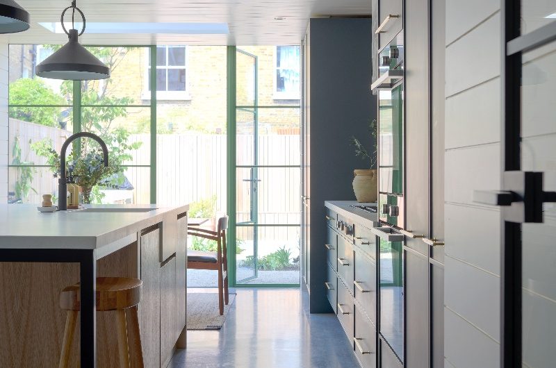 A coastal kitchen with run of cabinetry on the right and a central island, with steel-framed doors opening on to the garden.