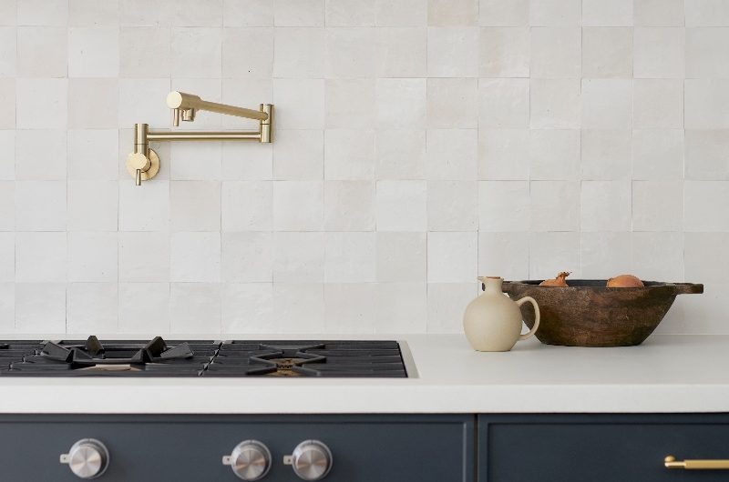 Closeup at a cooking zone with zellige wall tiles, a pot filler tap, hidden extractor, and a gas hob.